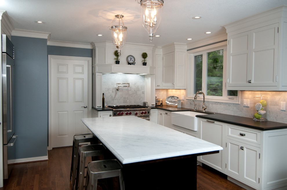 Kitchen - traditional l-shaped kitchen idea in Portland with stainless steel appliances, a farmhouse sink, recessed-panel cabinets, white cabinets, marble countertops, white backsplash and stone tile backsplash