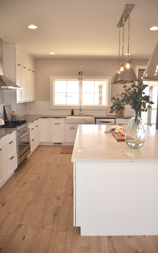 Bild på ett lantligt grå grått kök, med en rustik diskho, skåp i shakerstil, vita skåp, bänkskiva i kvarts, vitt stänkskydd, stänkskydd i tunnelbanekakel, rostfria vitvaror, vinylgolv och en köksö