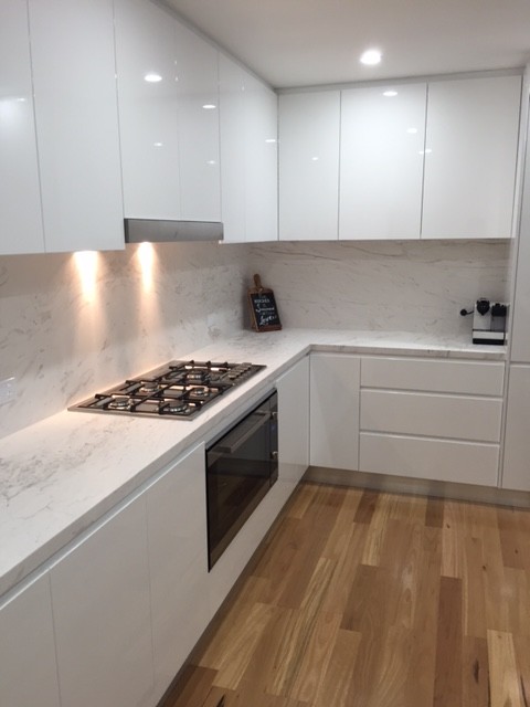 This is an example of a modern l-shaped kitchen/diner in Sydney with marble worktops, white splashback, stone slab splashback, flat-panel cabinets, white cabinets, stainless steel appliances and an island.