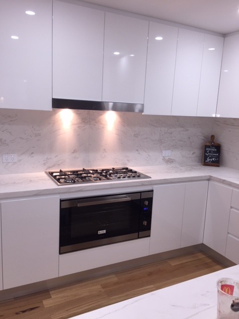 Exempel på ett modernt kök, med marmorbänkskiva, vitt stänkskydd, stänkskydd i sten, släta luckor, vita skåp, rostfria vitvaror, ljust trägolv och en köksö