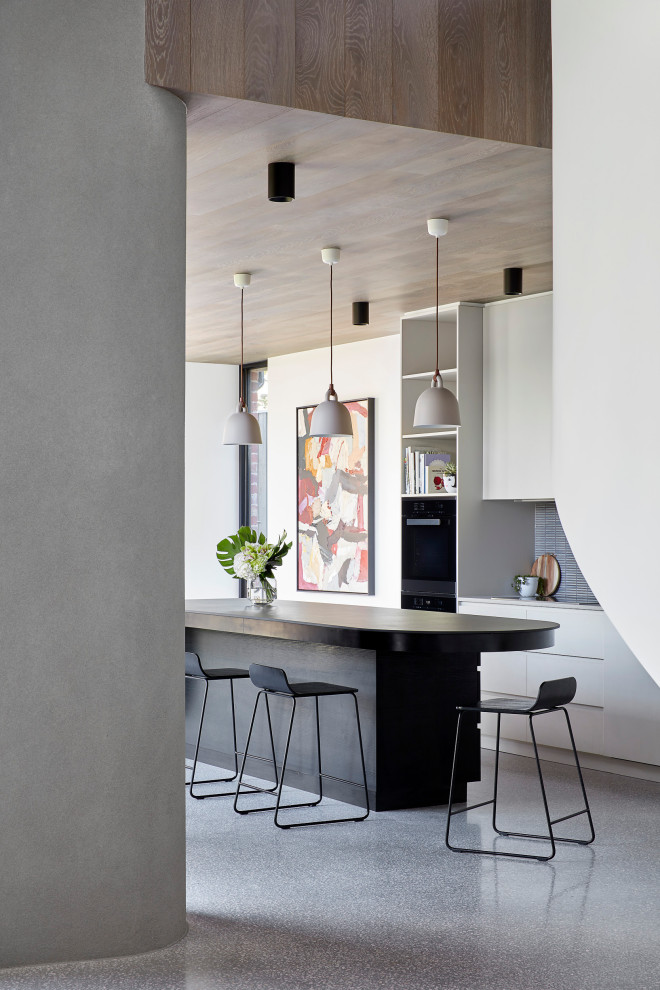 Mid-sized trendy galley concrete floor and gray floor eat-in kitchen photo in Melbourne with a drop-in sink, flat-panel cabinets, white cabinets, solid surface countertops, blue backsplash, ceramic backsplash, black appliances, an island and black countertops