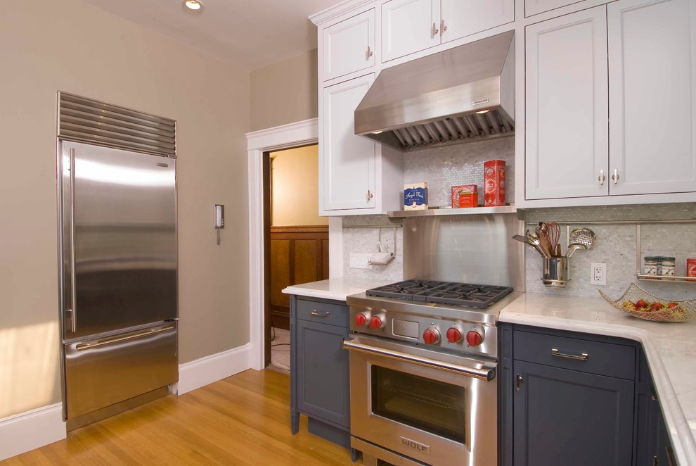 Inredning av ett modernt mellanstort kök, med en undermonterad diskho, skåp i shakerstil, blå skåp, bänkskiva i kvarts, grått stänkskydd, stänkskydd i glaskakel, rostfria vitvaror, ljust trägolv och en halv köksö