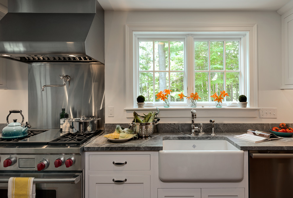Lantlig inredning av ett kök, med en rustik diskho, skåp i shakerstil, vita skåp, granitbänkskiva, stänkskydd med metallisk yta, stänkskydd i metallkakel och rostfria vitvaror