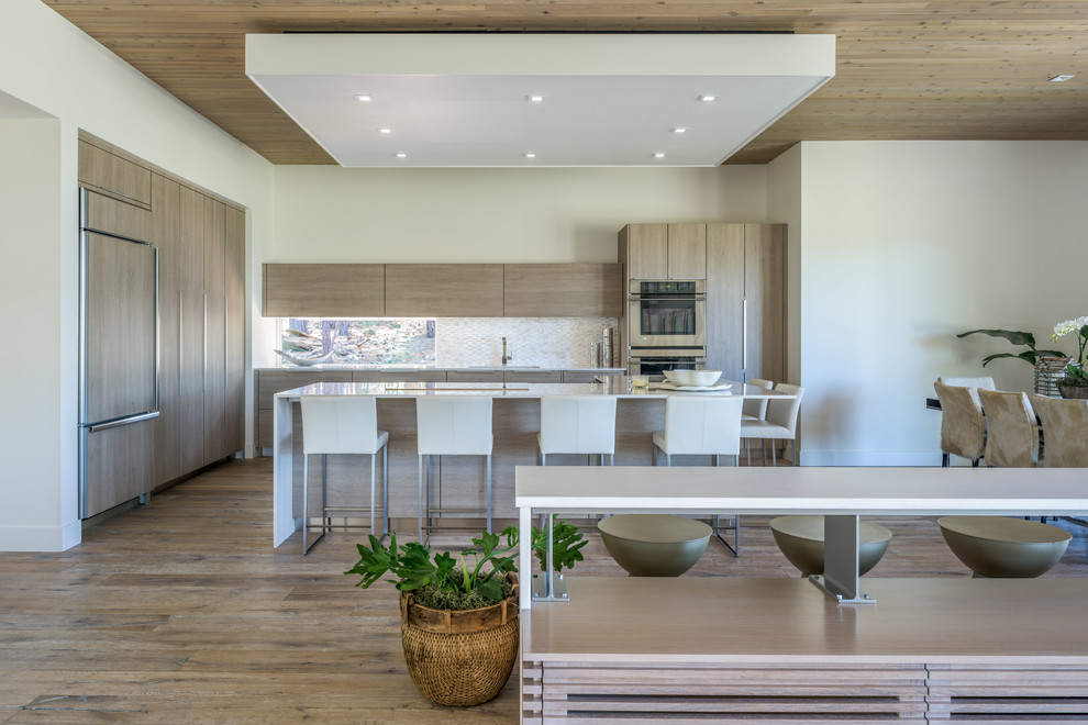 Photo of a contemporary open plan kitchen in Other with a submerged sink, flat-panel cabinets, medium wood cabinets, composite countertops, white splashback, metro tiled splashback, stainless steel appliances, medium hardwood flooring, an island and brown floors.