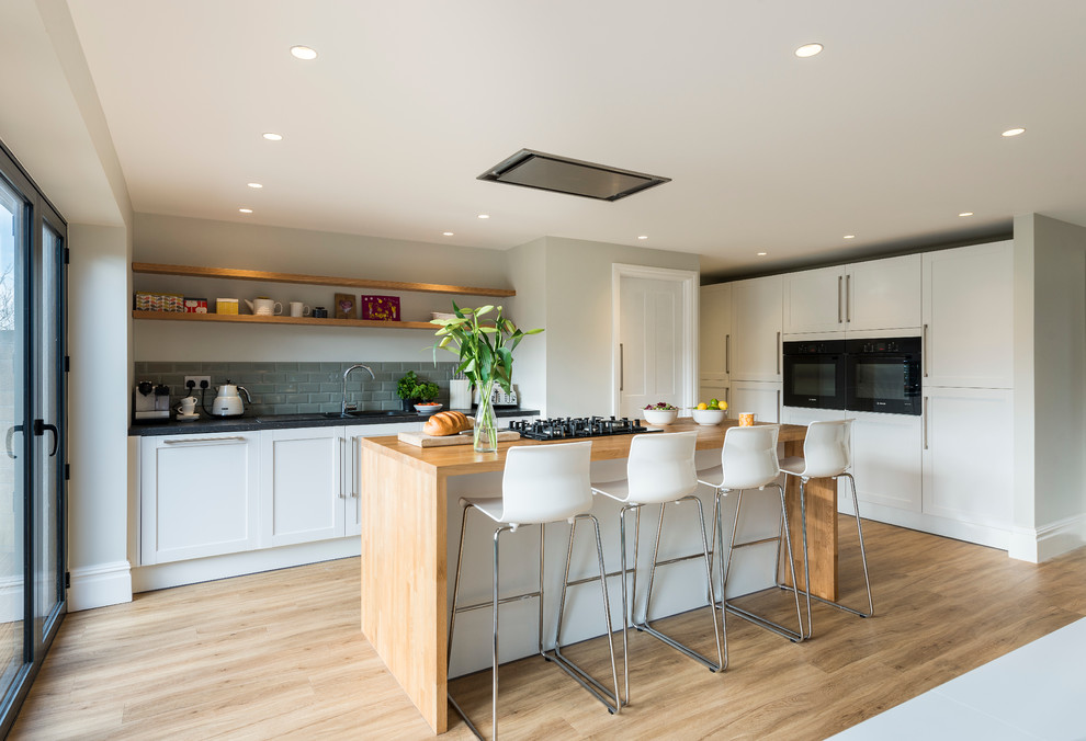 Klassische Küche mit Schrankfronten im Shaker-Stil, weißen Schränken, Küchenrückwand in Grau, Rückwand aus Metrofliesen, schwarzen Elektrogeräten, hellem Holzboden und Kücheninsel in London