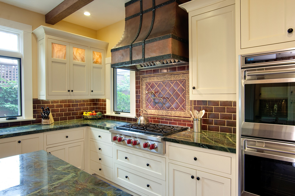 Example of a large arts and crafts u-shaped terra-cotta tile and brown floor eat-in kitchen design in San Diego with a farmhouse sink, raised-panel cabinets, white cabinets, marble countertops, brown backsplash, subway tile backsplash, stainless steel appliances and an island