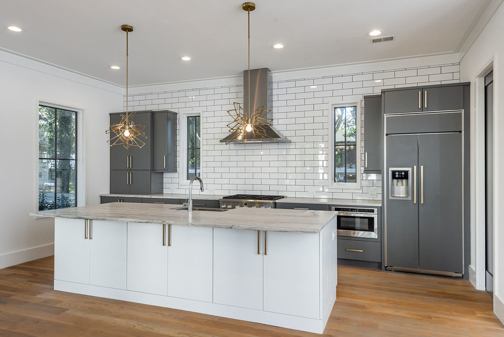 Inspiration for a mid-sized coastal galley medium tone wood floor and brown floor open concept kitchen remodel in Charleston with an undermount sink, gray cabinets, quartzite countertops, white backsplash, subway tile backsplash, paneled appliances, an island and multicolored countertops