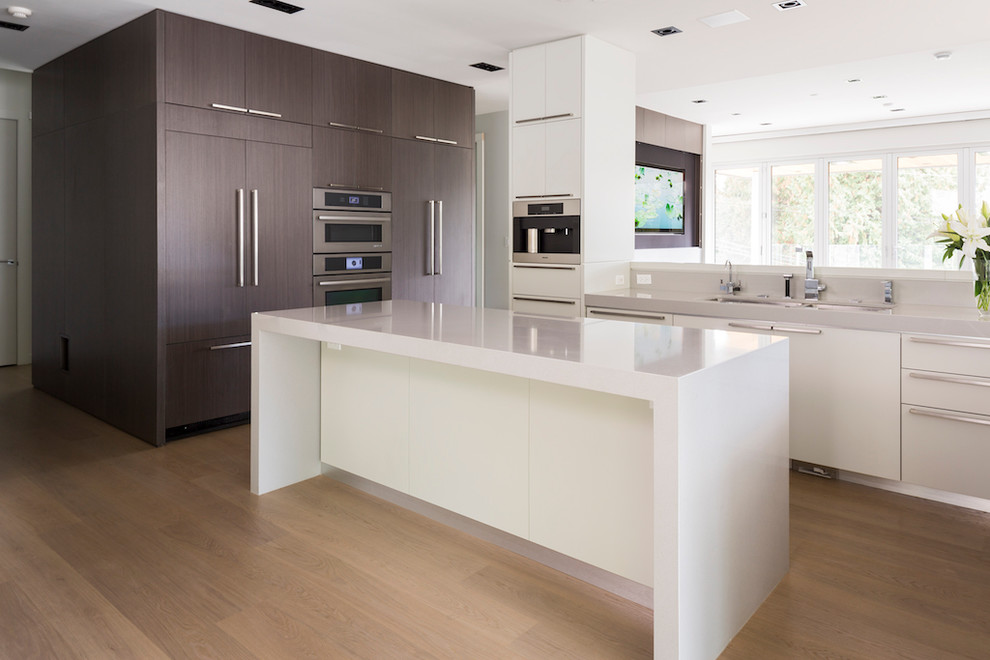 Moderne Wohnküche in L-Form mit Kücheninsel, flächenbündigen Schrankfronten, weißen Schränken, hellem Holzboden, Küchenrückwand in Grau, Elektrogeräten mit Frontblende, Quarzwerkstein-Arbeitsplatte und Unterbauwaschbecken in Vancouver