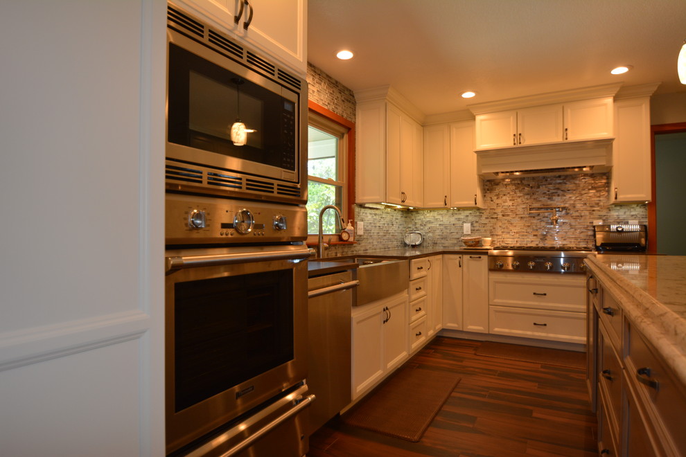Moderne Küche in L-Form mit Landhausspüle, Schrankfronten mit vertiefter Füllung, weißen Schränken, Granit-Arbeitsplatte, Küchenrückwand in Grau, Rückwand aus Mosaikfliesen, Küchengeräten aus Edelstahl, dunklem Holzboden und Kücheninsel in Tampa