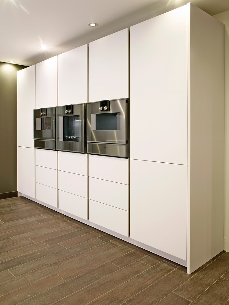 Foto de cocina contemporánea con armarios con paneles lisos, puertas de armario blancas, electrodomésticos de acero inoxidable, suelo de baldosas de cerámica y suelo marrón