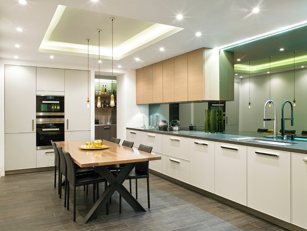 Exempel på ett stort modernt kök och matrum, med en undermonterad diskho, släta luckor, vita skåp, granitbänkskiva, stänkskydd med metallisk yta, spegel som stänkskydd, rostfria vitvaror, klinkergolv i keramik och grått golv