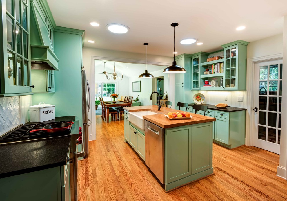 Eat-in kitchen - small 1950s galley medium tone wood floor and brown floor eat-in kitchen idea in Raleigh with a farmhouse sink, shaker cabinets, turquoise cabinets, granite countertops, white backsplash, porcelain backsplash, stainless steel appliances, an island and black countertops