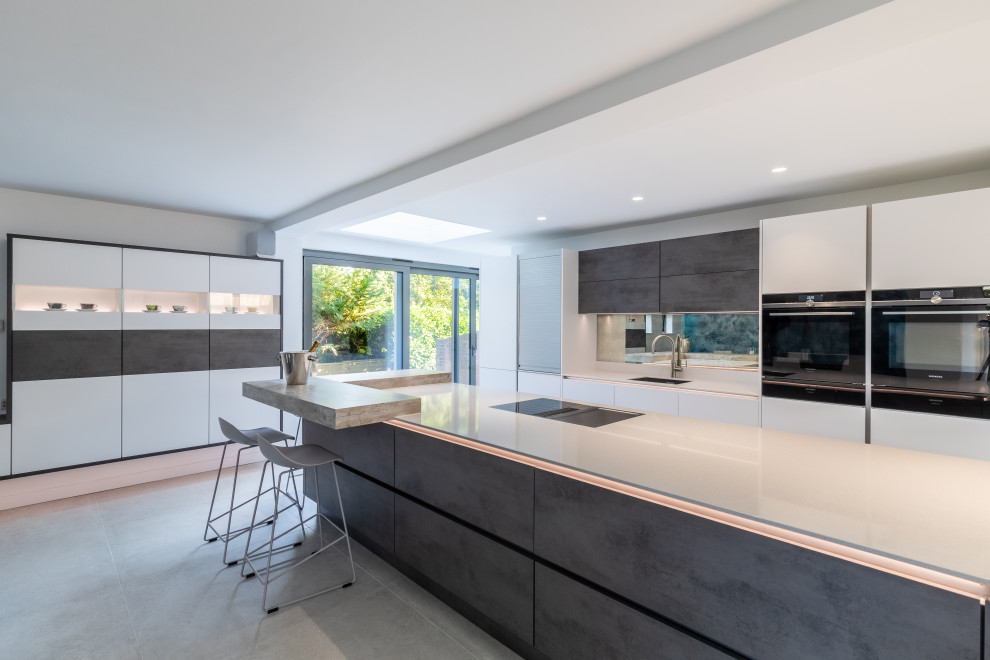Design ideas for a large contemporary single-wall kitchen/diner in Hampshire with a single-bowl sink, flat-panel cabinets, white cabinets, quartz worktops, multi-coloured splashback, mirror splashback, black appliances, ceramic flooring, an island, grey floors and white worktops.