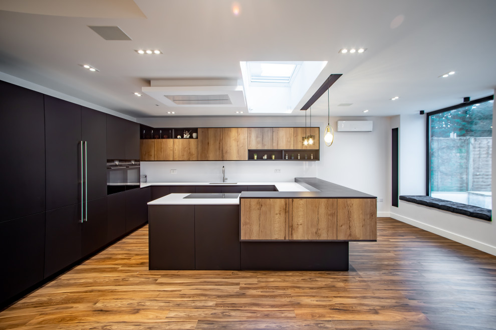 Mid-sized trendy u-shaped dark wood floor and brown floor eat-in kitchen photo in London with a drop-in sink, beaded inset cabinets, black cabinets, quartzite countertops, white backsplash, ceramic backsplash, black appliances, an island and black countertops