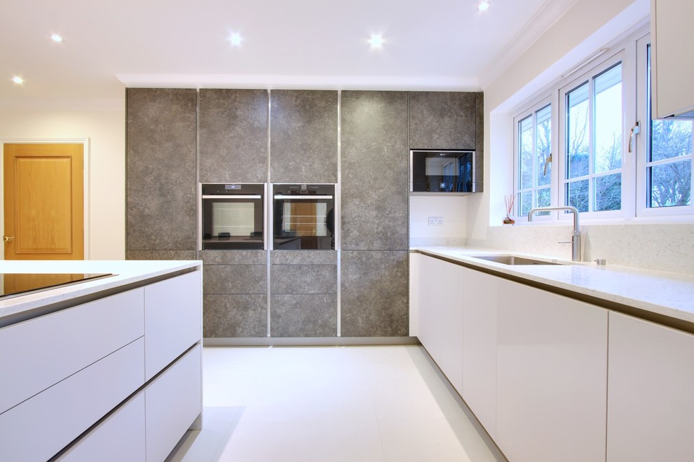 Design ideas for a medium sized contemporary u-shaped kitchen/diner in Hertfordshire with a submerged sink, flat-panel cabinets, white cabinets, quartz worktops, white splashback, stone slab splashback, black appliances and an island.