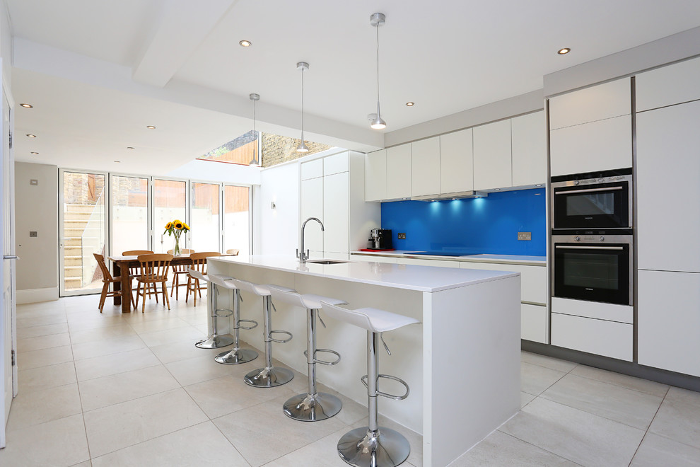 Foto di una cucina minimal con ante lisce, ante bianche, paraspruzzi blu, paraspruzzi con lastra di vetro, elettrodomestici in acciaio inossidabile e pavimento in gres porcellanato