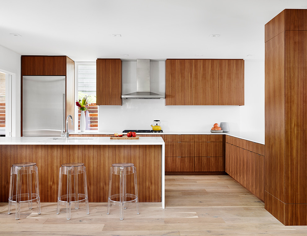 Contemporary l-shaped kitchen in Austin with flat-panel cabinets, medium wood cabinets, marble worktops, white splashback, stainless steel appliances, light hardwood flooring, an island and a submerged sink.