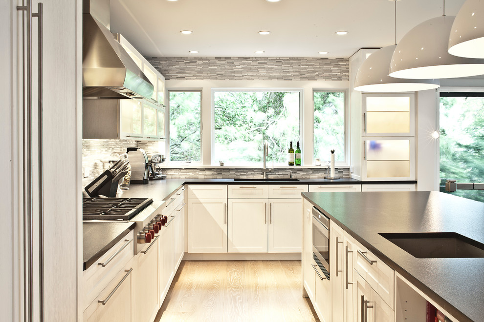 Inspiration for a large contemporary u-shaped light wood floor eat-in kitchen remodel in New York with an undermount sink, glass-front cabinets, white cabinets, gray backsplash, stainless steel appliances and an island