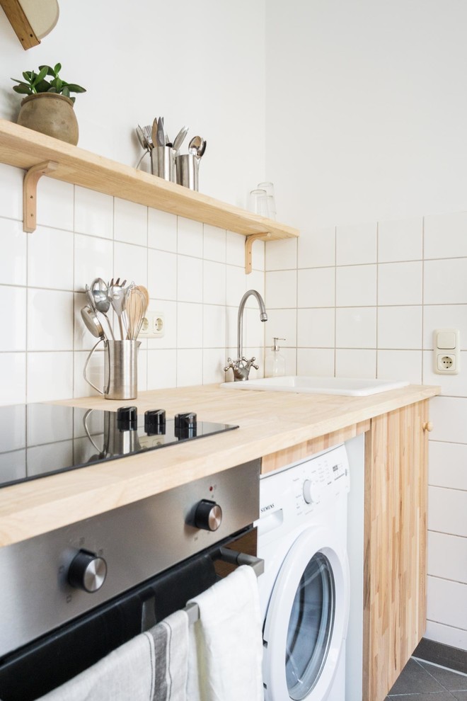 ベルリンにある小さな北欧スタイルのおしゃれなキッチン (ドロップインシンク、フラットパネル扉のキャビネット、淡色木目調キャビネット、木材カウンター、白いキッチンパネル、シルバーの調理設備、グレーの床、ベージュのキッチンカウンター、セラミックタイルのキッチンパネル、アイランドなし) の写真