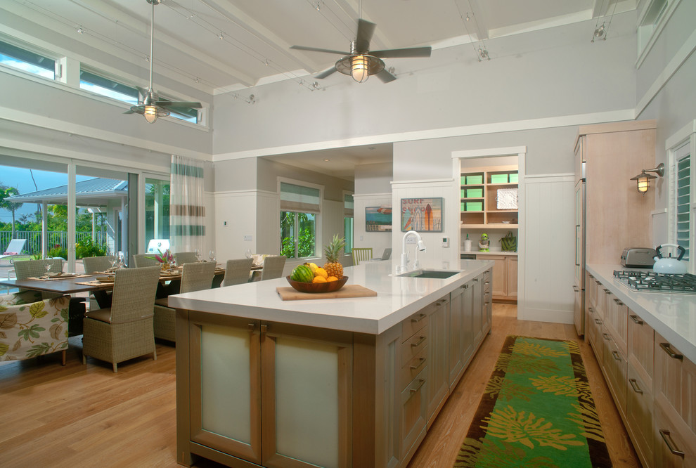 Inspiration for a large world-inspired single-wall kitchen/diner in Hawaii with light hardwood flooring, brown floors, a submerged sink, stainless steel appliances, recessed-panel cabinets, light wood cabinets, engineered stone countertops and an island.