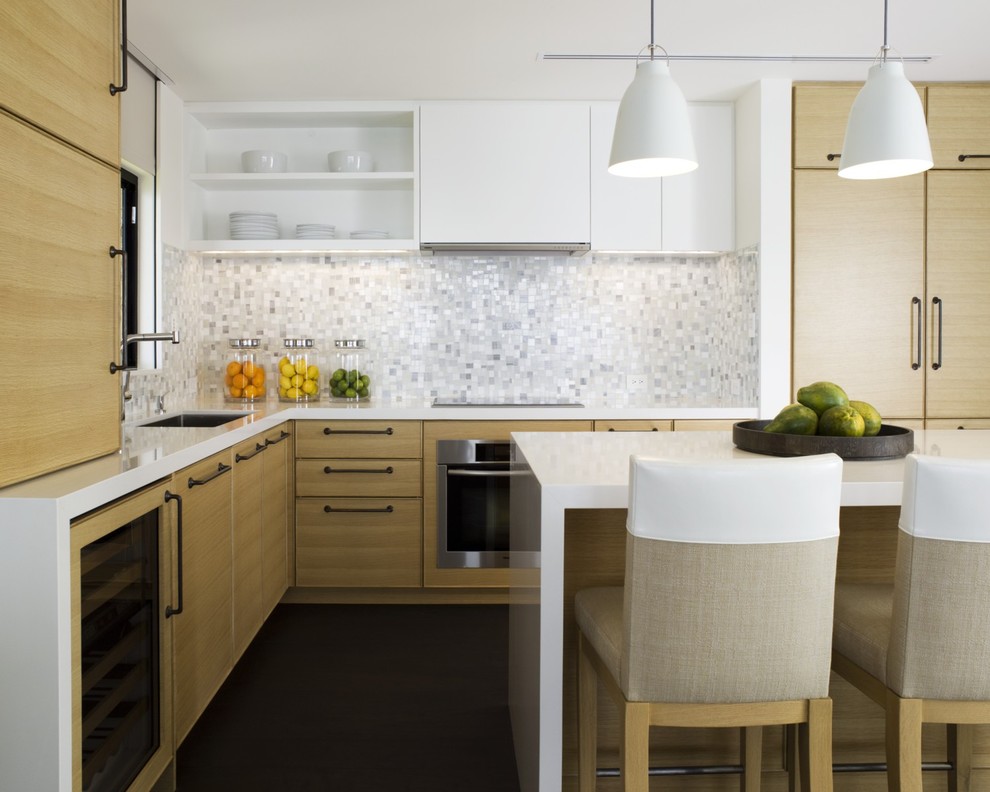На фото: кухня в современном стиле с белым фартуком, плоскими фасадами, светлыми деревянными фасадами и барной стойкой