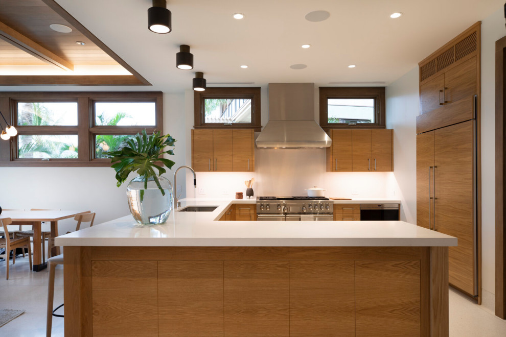 This is an example of a world-inspired u-shaped kitchen in Los Angeles with a submerged sink, flat-panel cabinets, medium wood cabinets, integrated appliances, a breakfast bar, grey floors and white worktops.