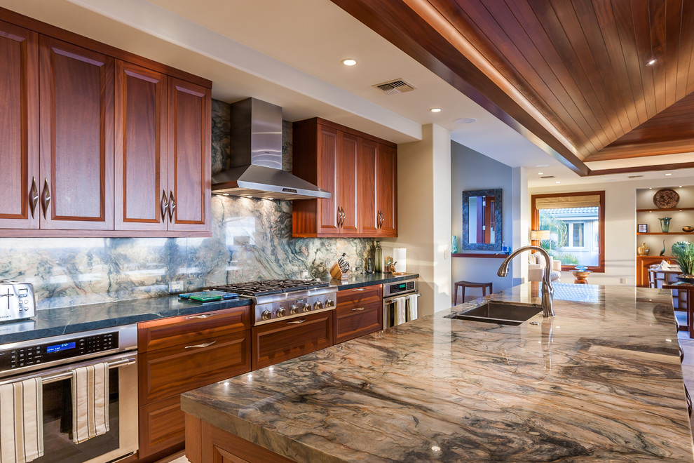 Inspiration for a large tropical travertine floor kitchen remodel in Hawaii with recessed-panel cabinets, quartzite countertops, green backsplash, glass tile backsplash, stainless steel appliances and two islands