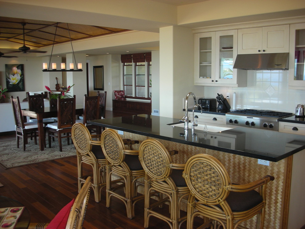 На фото: кухня-гостиная в морском стиле с стеклянными фасадами, гранитной столешницей и белым фартуком