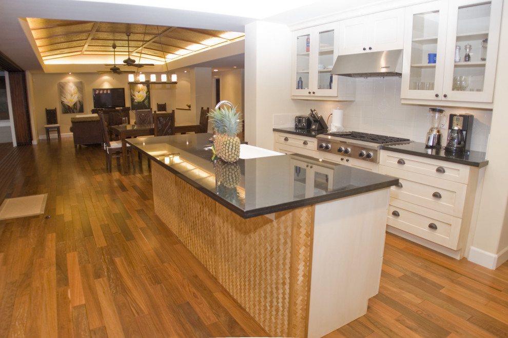 Example of an island style kitchen design in Hawaii with glass-front cabinets, white cabinets and white backsplash