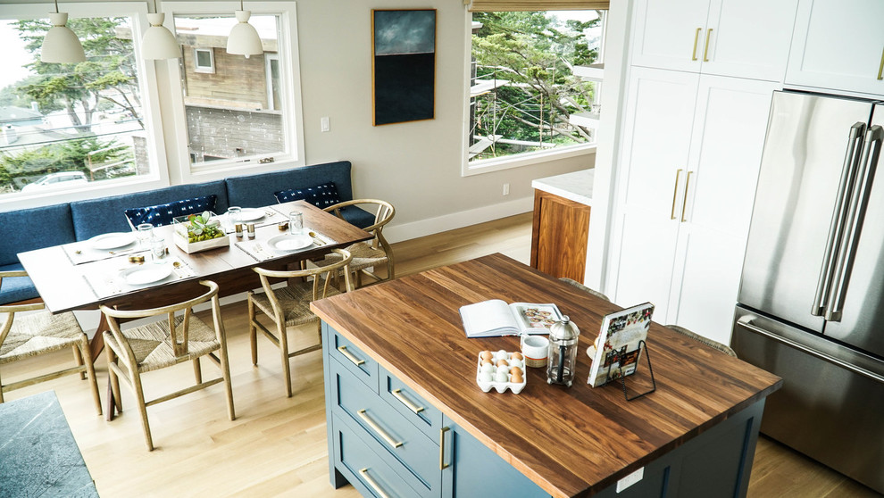 Bild på ett maritimt kök, med skåp i shakerstil, blå skåp, bänkskiva i täljsten, stänkskydd i keramik, rostfria vitvaror, ljust trägolv och en köksö
