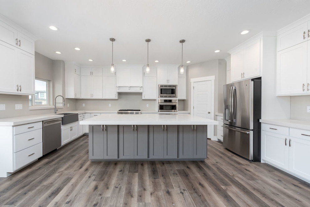 Large traditional u-shaped open plan kitchen in Salt Lake City with a belfast sink, shaker cabinets, grey cabinets, granite worktops, stainless steel appliances, laminate floors, an island, grey floors and white worktops.