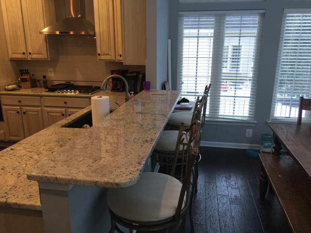 This is an example of a medium sized traditional u-shaped open plan kitchen in DC Metro with a submerged sink, raised-panel cabinets, white cabinets, granite worktops, black appliances, dark hardwood flooring, an island, brown floors and grey worktops.