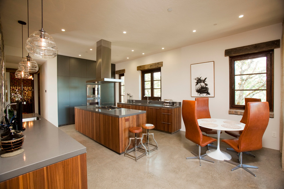 Large urban u-shaped concrete floor enclosed kitchen photo in San Francisco with an undermount sink, flat-panel cabinets, medium tone wood cabinets, solid surface countertops, stainless steel appliances and an island