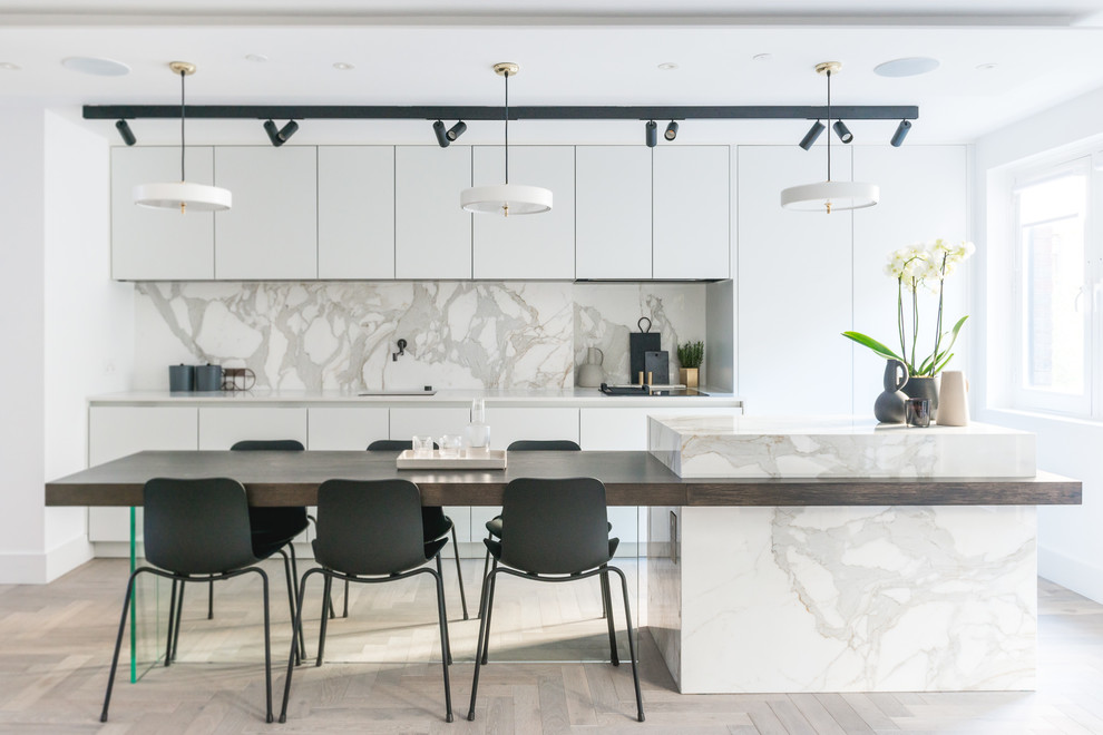 Medium sized contemporary single-wall open plan kitchen in London with a submerged sink, flat-panel cabinets, white cabinets, marble worktops, grey splashback, marble splashback, black appliances, light hardwood flooring, an island and grey floors.