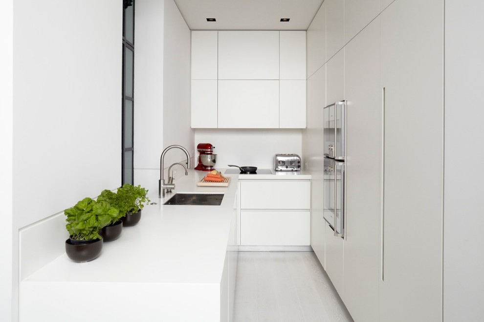 Идея дизайна: узкая отдельная, угловая кухня в стиле модернизм с врезной мойкой, плоскими фасадами, белыми фасадами, техникой под мебельный фасад и белым фартуком