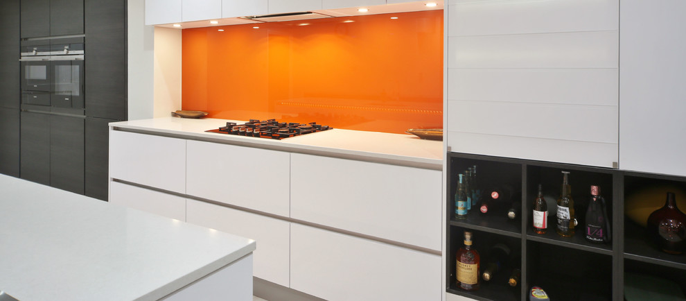 ロンドンにあるお手頃価格の中くらいなコンテンポラリースタイルのおしゃれなキッチン (アンダーカウンターシンク、フラットパネル扉のキャビネット、白いキャビネット、珪岩カウンター、オレンジのキッチンパネル、ガラス板のキッチンパネル、黒い調理設備、磁器タイルの床、ベージュの床、白いキッチンカウンター) の写真