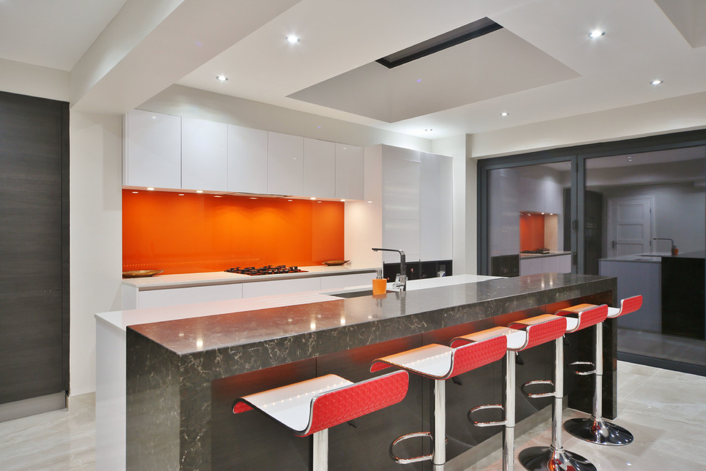 ロンドンにあるお手頃価格の中くらいなコンテンポラリースタイルのおしゃれなキッチン (アンダーカウンターシンク、フラットパネル扉のキャビネット、白いキャビネット、珪岩カウンター、オレンジのキッチンパネル、ガラス板のキッチンパネル、黒い調理設備、磁器タイルの床、ベージュの床、白いキッチンカウンター) の写真