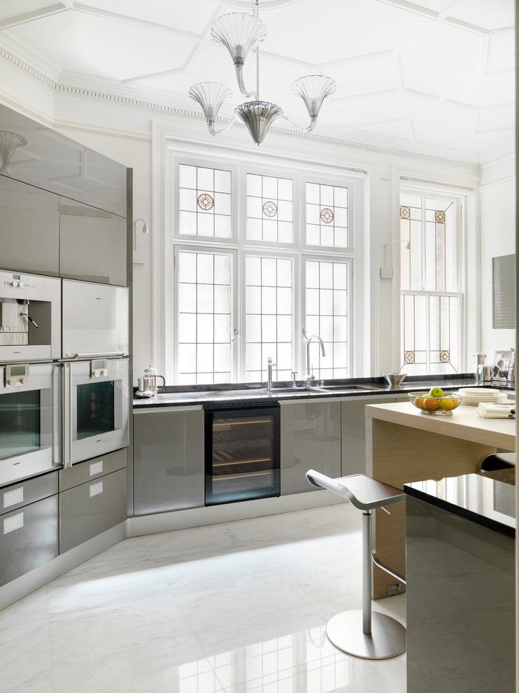 Ejemplo de cocina contemporánea grande con puertas de armario grises, electrodomésticos de acero inoxidable, suelo de mármol, fregadero de doble seno y armarios con paneles lisos