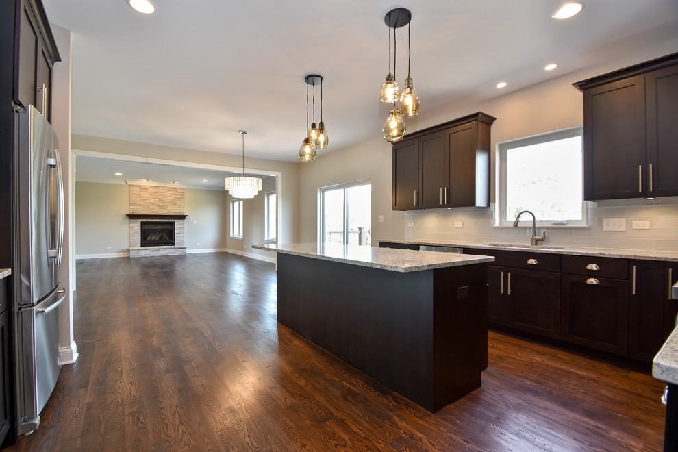 Large classic u-shaped open plan kitchen in Chicago with recessed-panel cabinets, dark wood cabinets, white splashback, glass tiled splashback, stainless steel appliances, dark hardwood flooring, an island and a submerged sink.