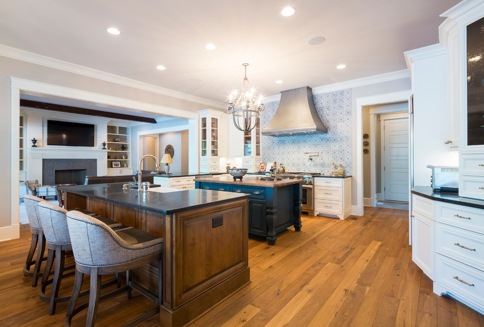 Inspiration for a huge rustic medium tone wood floor eat-in kitchen remodel in Charlotte with a farmhouse sink, raised-panel cabinets, white cabinets, blue backsplash, mosaic tile backsplash, stainless steel appliances and two islands