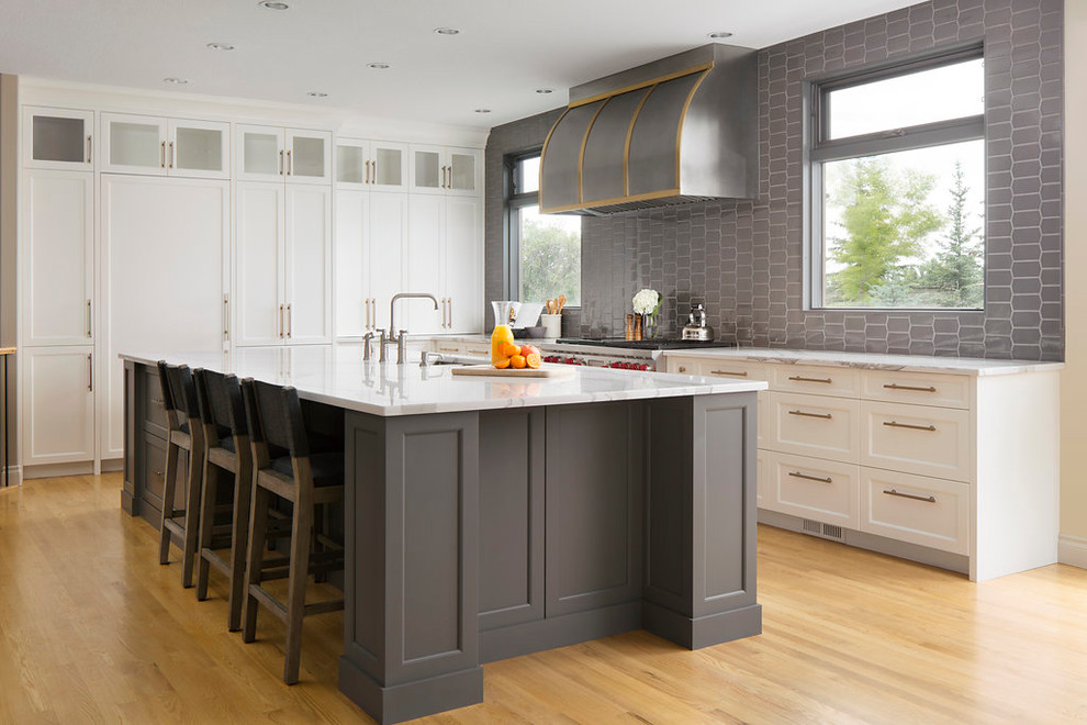 Idéer för ett stort klassiskt linjärt kök med öppen planlösning, med en undermonterad diskho, skåp i shakerstil, vita skåp, grått stänkskydd, rostfria vitvaror, ljust trägolv, en köksö, marmorbänkskiva, stänkskydd i keramik och brunt golv