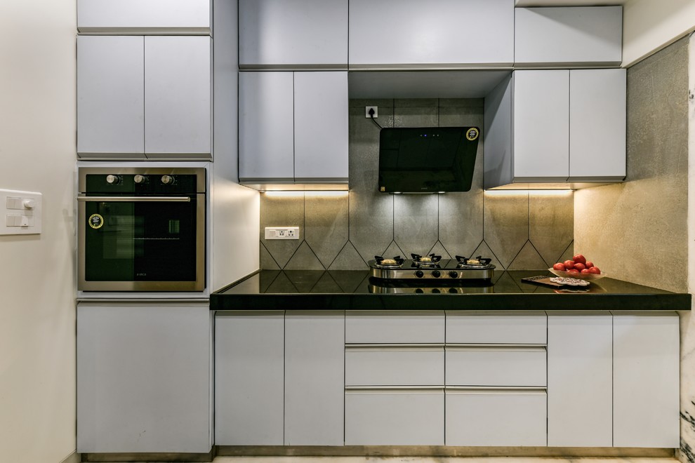 Inspiration for a contemporary kitchen in Mumbai with flat-panel cabinets, grey cabinets, grey splashback, stainless steel appliances, black worktops and granite worktops.