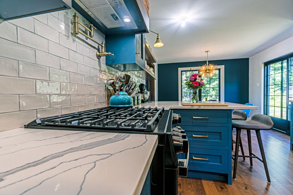 Bild på ett mellanstort eklektiskt grå grått kök och matrum, med en rustik diskho, skåp i shakerstil, blå skåp, granitbänkskiva, vitt stänkskydd, stänkskydd i keramik, rostfria vitvaror, mellanmörkt trägolv, en halv köksö och brunt golv