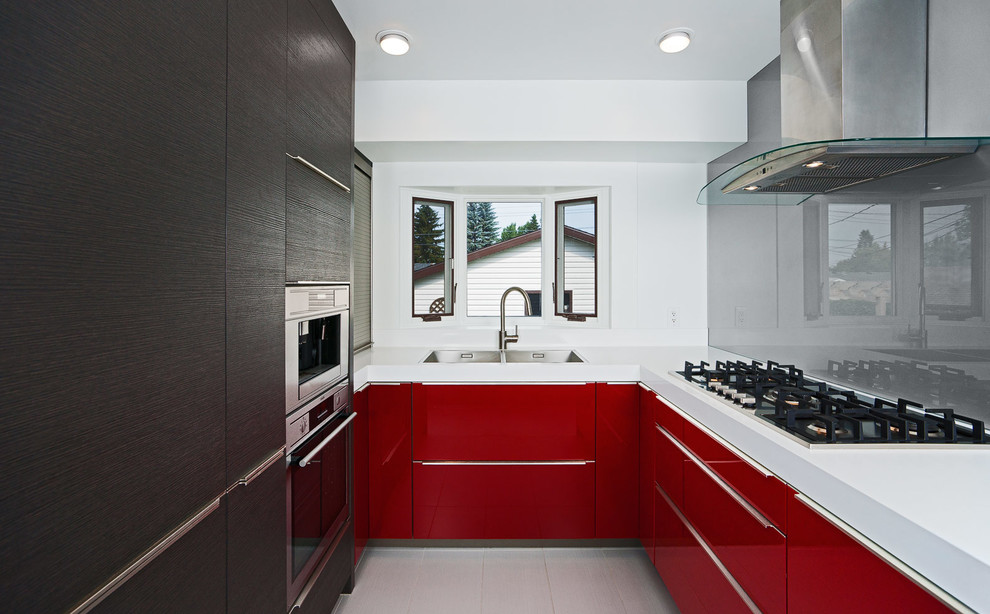 Bild på ett avskilt funkis u-kök, med en nedsänkt diskho, släta luckor, röda skåp, bänkskiva i kvarts, stänkskydd med metallisk yta, glaspanel som stänkskydd och integrerade vitvaror