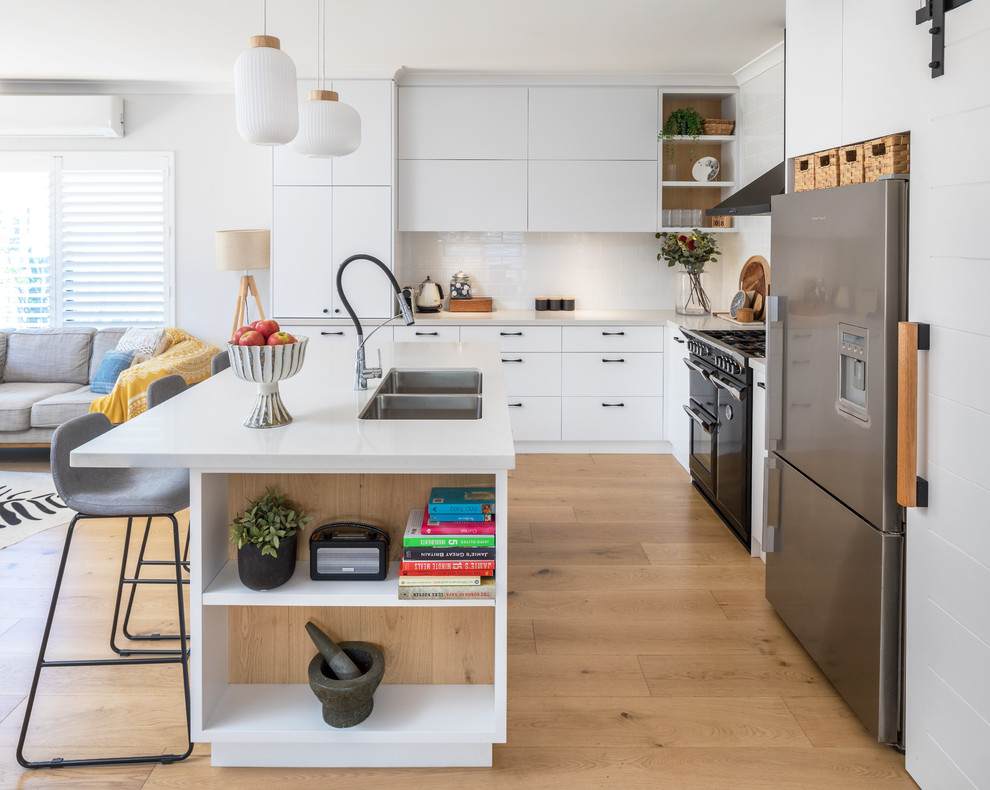This is an example of a modern kitchen in Perth with flat-panel cabinets, white cabinets, engineered stone countertops, white splashback, metro tiled splashback, medium hardwood flooring, an island, white worktops, a double-bowl sink, stainless steel appliances and brown floors.