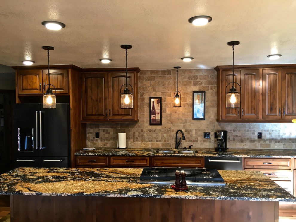 Große Küche in L-Form mit Vorratsschrank, Unterbauwaschbecken, profilierten Schrankfronten, Granit-Arbeitsplatte, Rückwand aus Travertin, schwarzen Elektrogeräten, hellem Holzboden und Kücheninsel in Denver