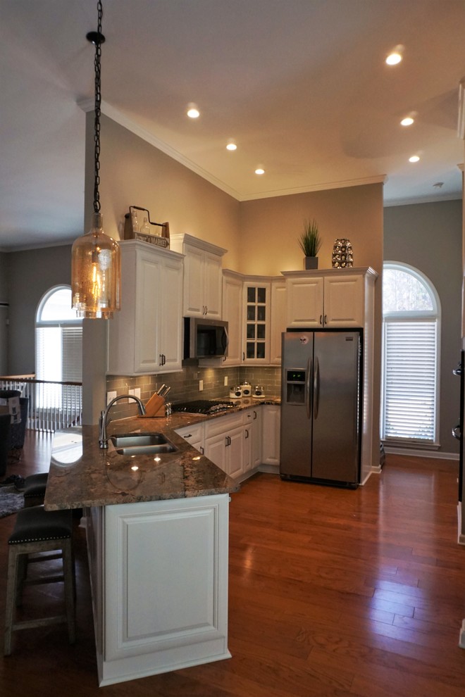 Medium sized classic galley open plan kitchen in Atlanta with a double-bowl sink, raised-panel cabinets, white cabinets, granite worktops, grey splashback, glass tiled splashback, stainless steel appliances, medium hardwood flooring, a breakfast bar and red floors.