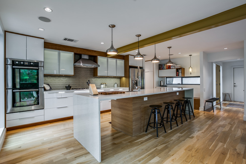 Foto di una cucina design con ante lisce, ante bianche, paraspruzzi grigio, elettrodomestici in acciaio inossidabile, pavimento in legno massello medio, pavimento marrone e top bianco