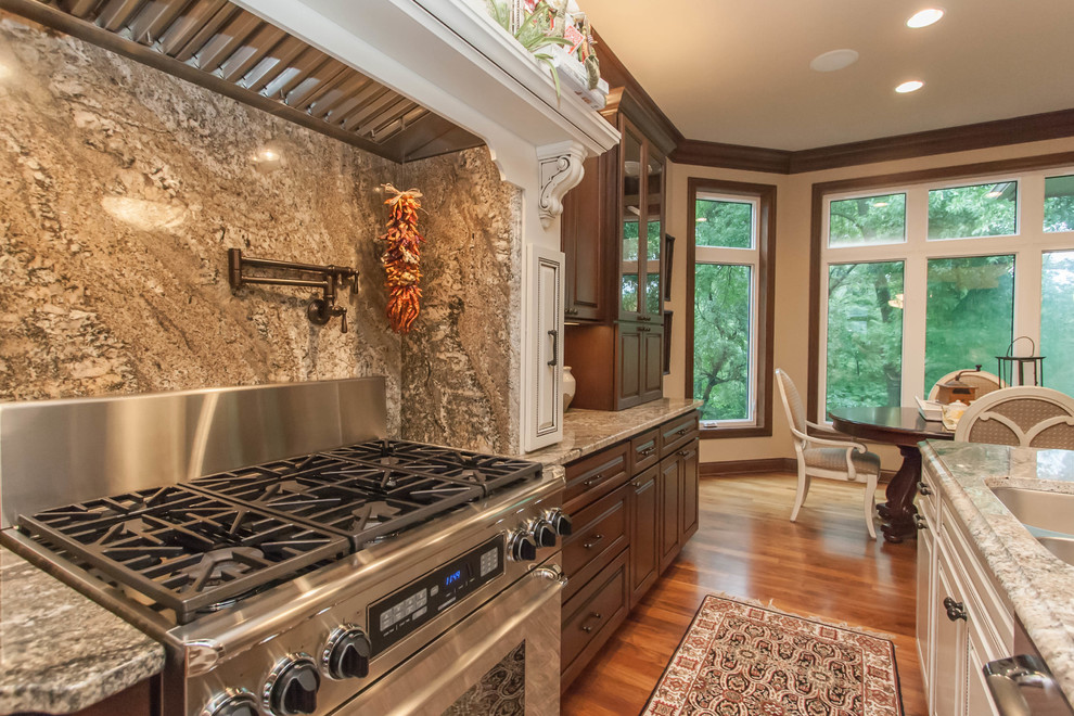 Exemple d'une grande cuisine américaine chic en U et bois foncé avec un plan de travail en granite, une crédence beige, un électroménager en acier inoxydable, un sol en bois brun et îlot.