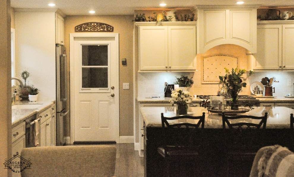 Example of a mid-sized transitional single-wall eat-in kitchen design in Los Angeles with an undermount sink, recessed-panel cabinets, white cabinets, granite countertops, beige backsplash, ceramic backsplash, stainless steel appliances and an island